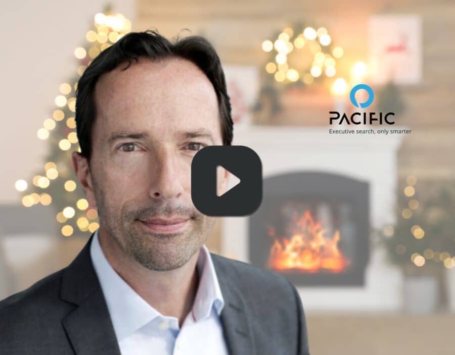 Man in a suit poses in front of a fireplace with holiday decorations; Pacific logo and slogan "Executive search, only smarter" appear on the wall, capturing the spirit of going Beyond Resilience this festive season.