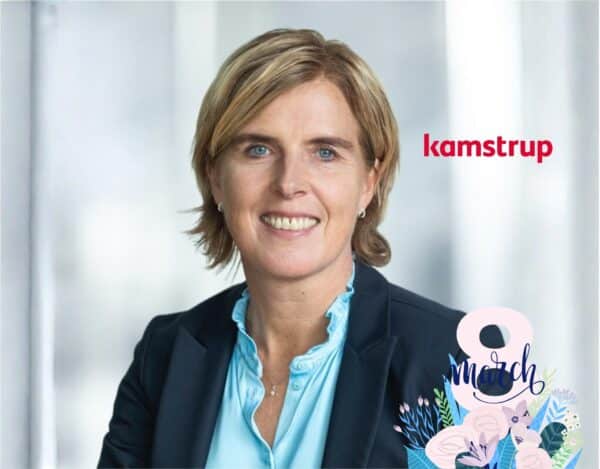 A woman in business attire smiles at the camera, with the "kamstrup" logo and a "8 March" floral graphic in the foreground.