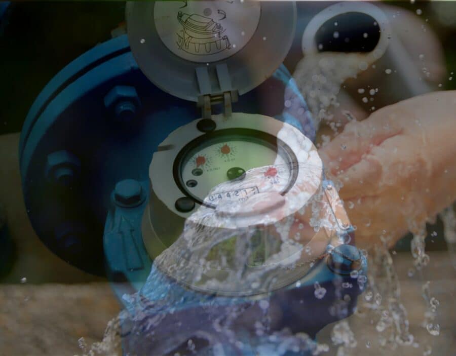 A close-up of a water meter with running water and hands being washed in the background, symbolising water usage measurement and hygiene.